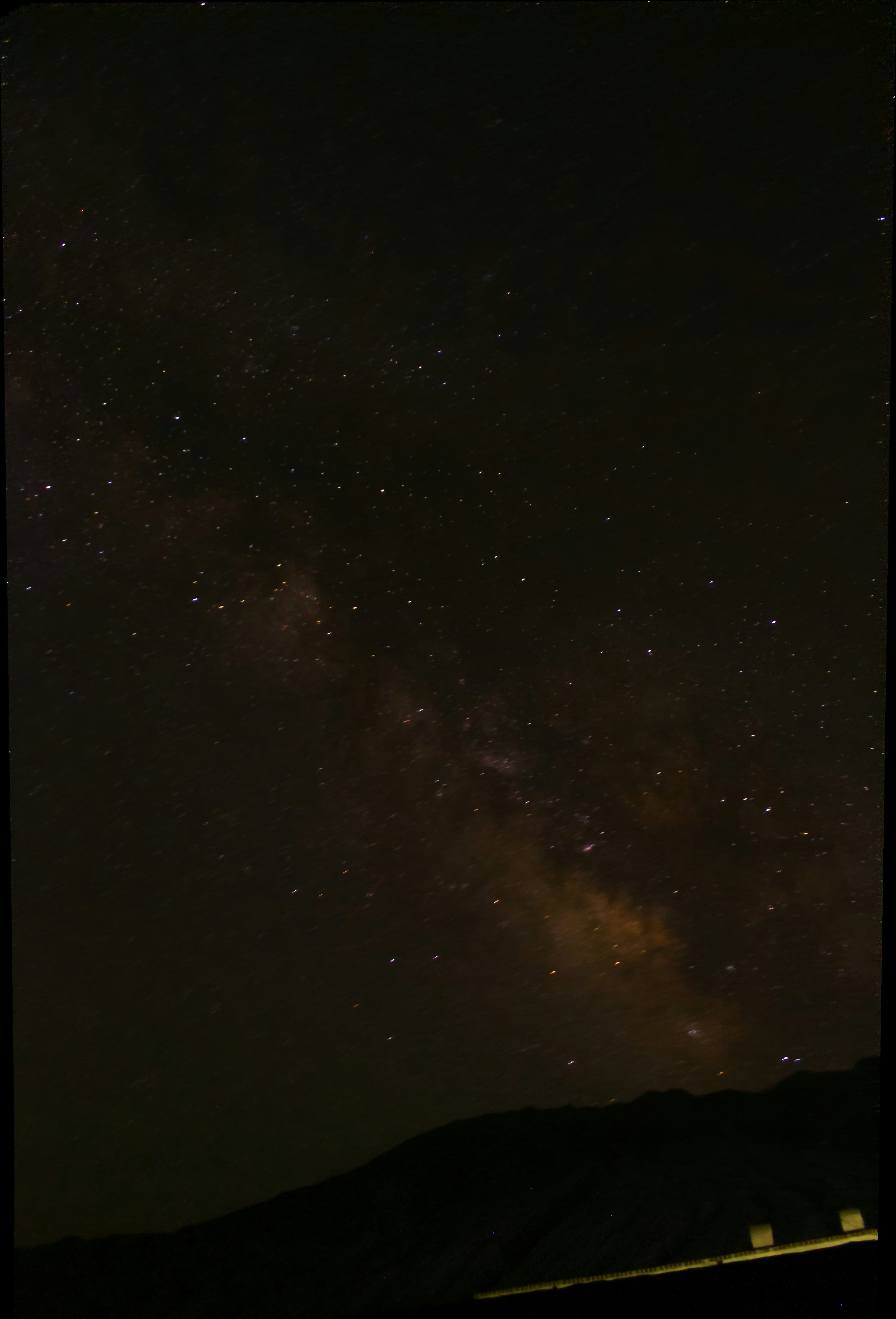 A star-filled night sky above a dark mountain horizon
